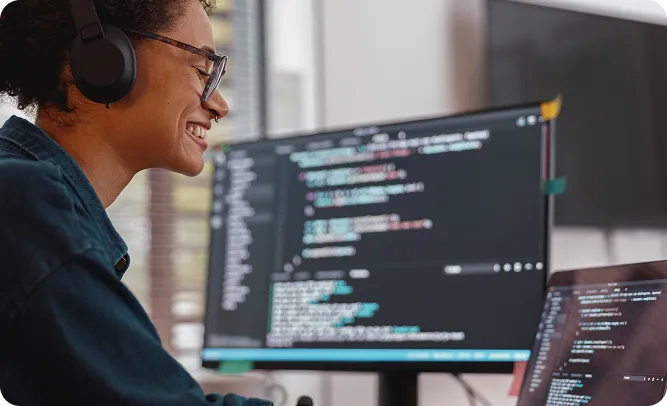 Desenvolvedora sorrindo em frente a monitores com código