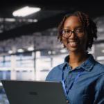 Happy woman in data center doing maintenance tasks on laptop, ensuring optimal performance. Engineering team reviewing diagnostics and applying patches to server room, improving stability