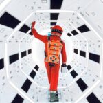 Scene from the movie 2001: A Space Odyssey; an Astronaut walking in a futuristic corridor with a geometric design and bright lighting.
