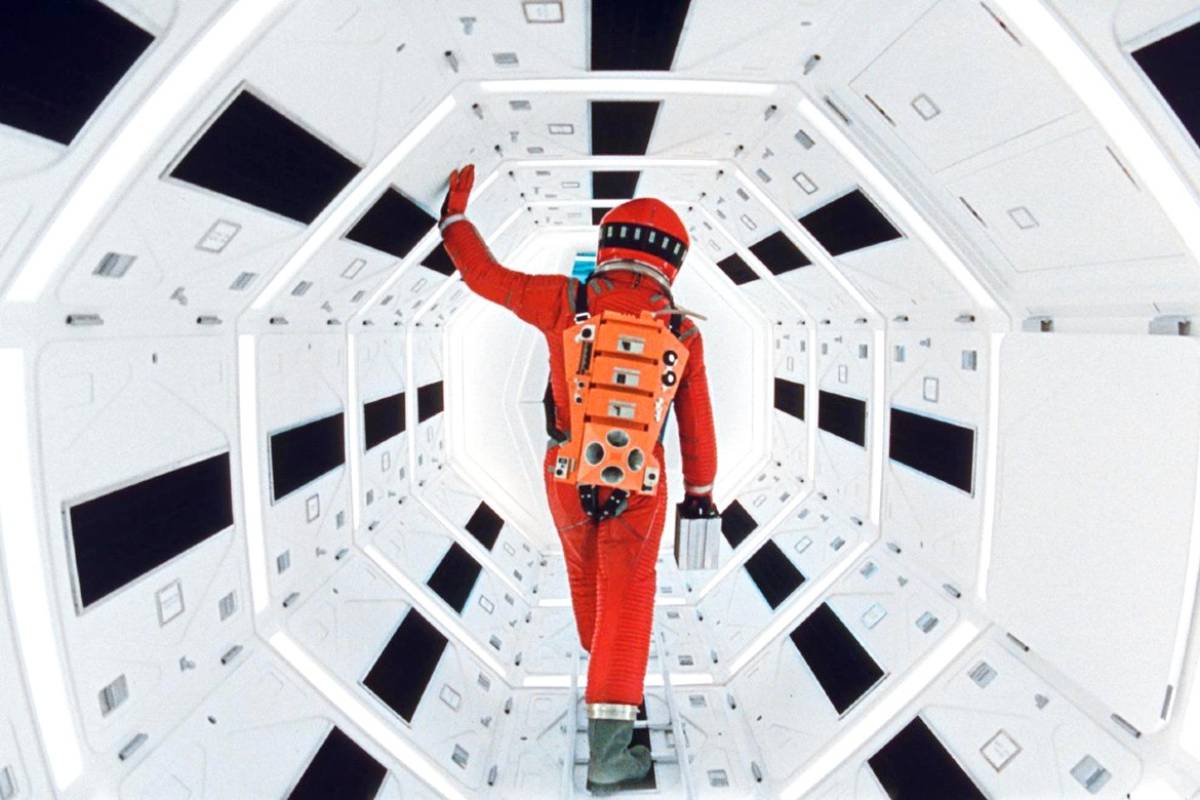 Cena do filme 2001: Uma Odisseia no Espaço; Astronauta caminhando em um corredor futurista com design geométrico e iluminação brilhante.