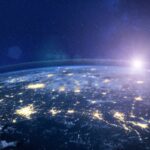 Nighttime aerial view of Earth, highlighting city lights and a sunrise on the horizon.
