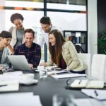 Equipe diversificada reunida ao redor de um laptop, colaborando em um ambiente corporativo moderno.