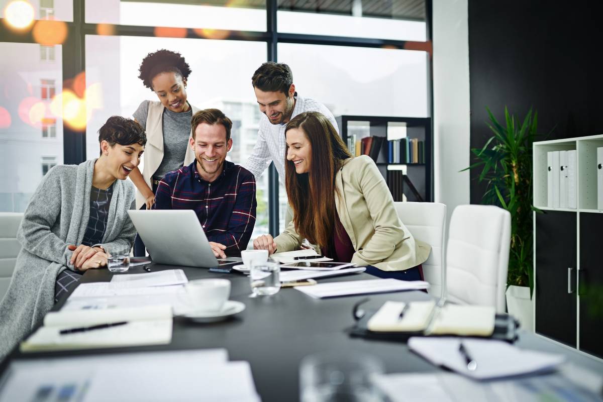 Equipe diversificada reunida ao redor de um laptop, colaborando em um ambiente corporativo moderno.