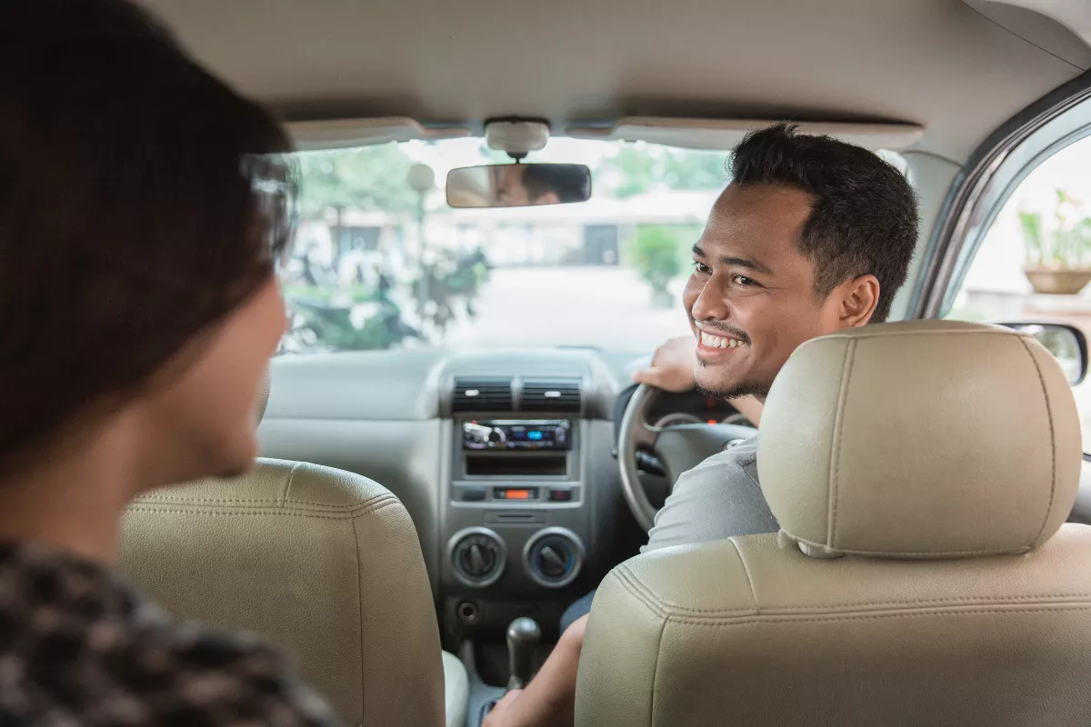 Motorista de aplicativo sorrindo para passageira dentro do carro, simbolizando inovação no transporte.