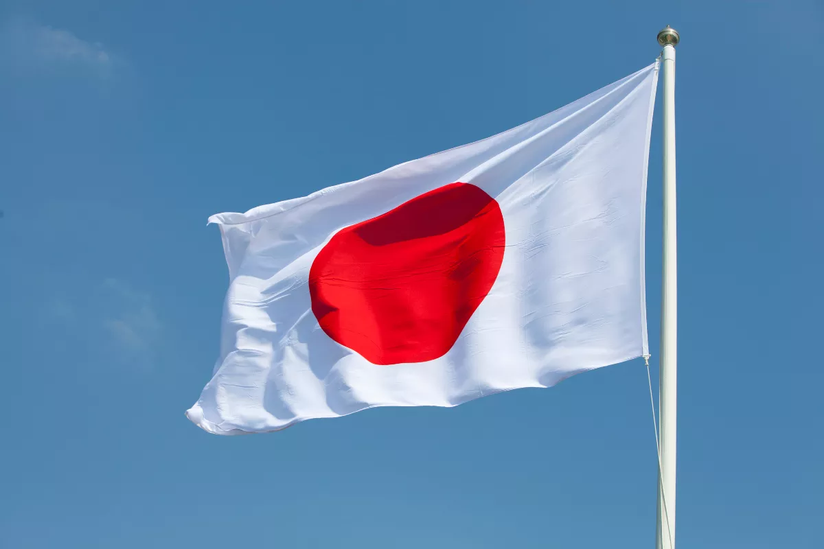 Japanese flag waving against a blue sky. The image symbolizes the origins of Lean Methodology, which was born in Japan within the Toyota Production System (TPS). It represents Japanese innovation in process management and waste elimination.