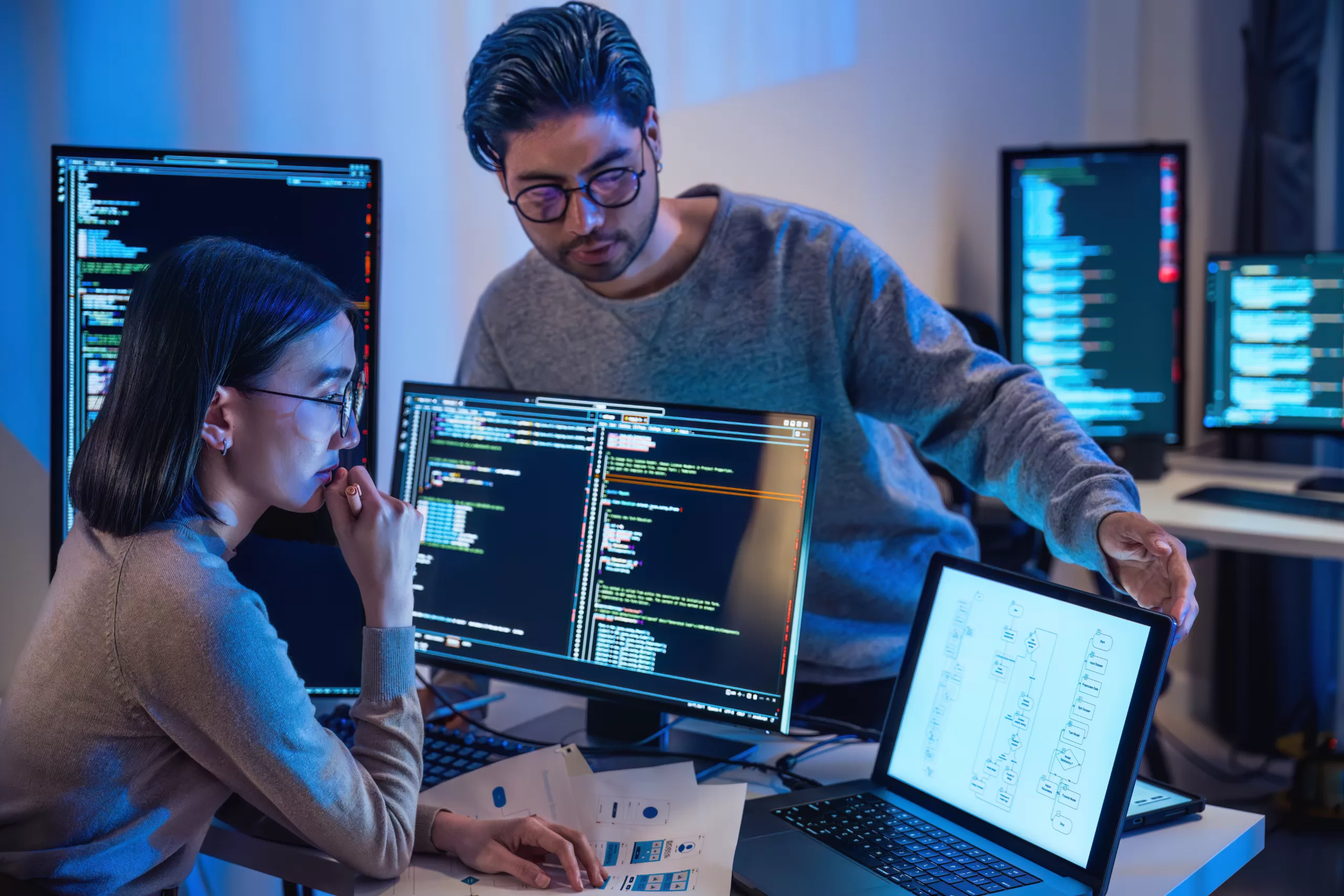 Dois desenvolvedores conversando na frente de um computador mostrando códigos 