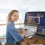 Imagem de uma mulher loira na frente de um computador trabalhando em uma fábrica de software