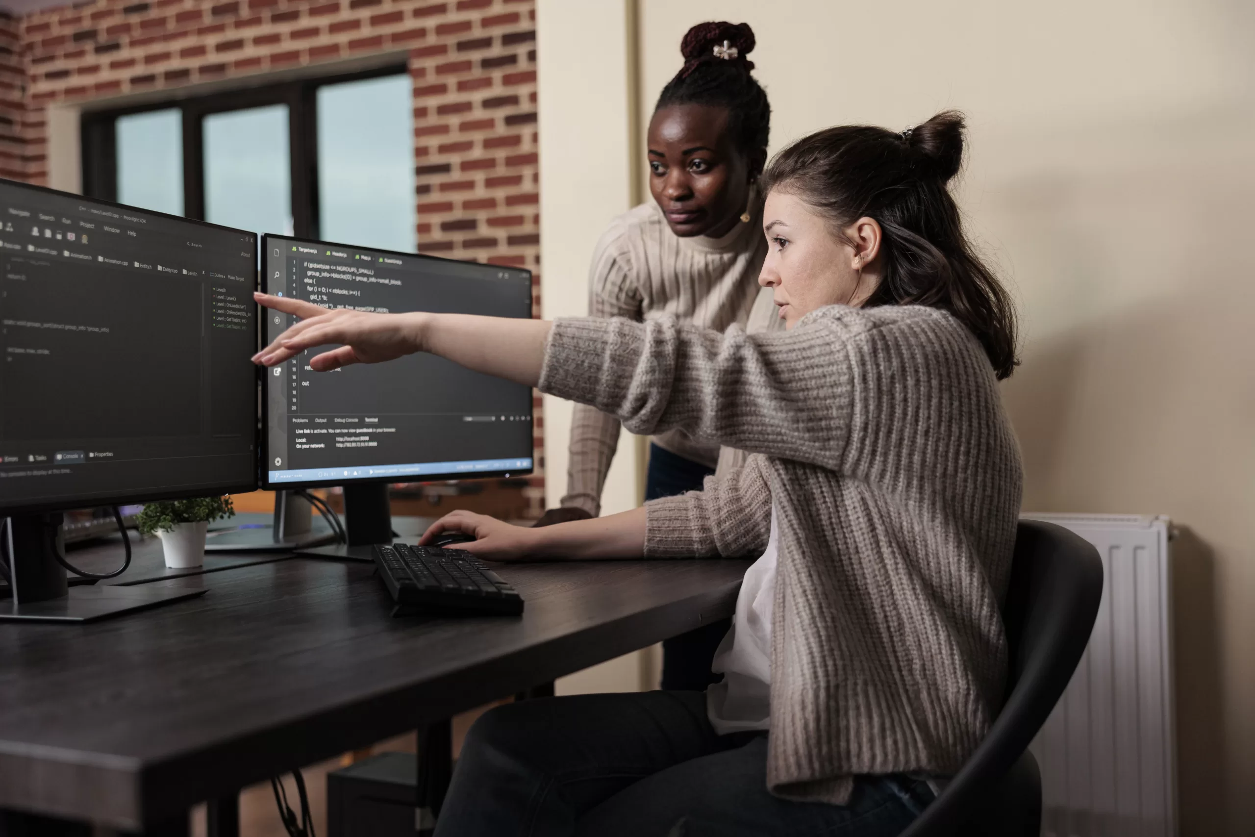 Imagem de duas mulheres discutindo uma ideia na frente de uma tela do computador 