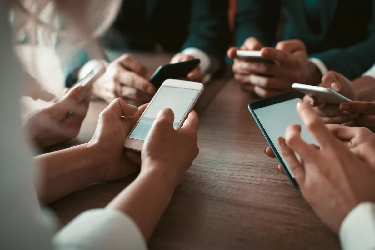 Grupo de pessoas usando smartphones ao redor de uma mesa, simbolizando a colaboração e o uso empresarial de aplicativos móveis.