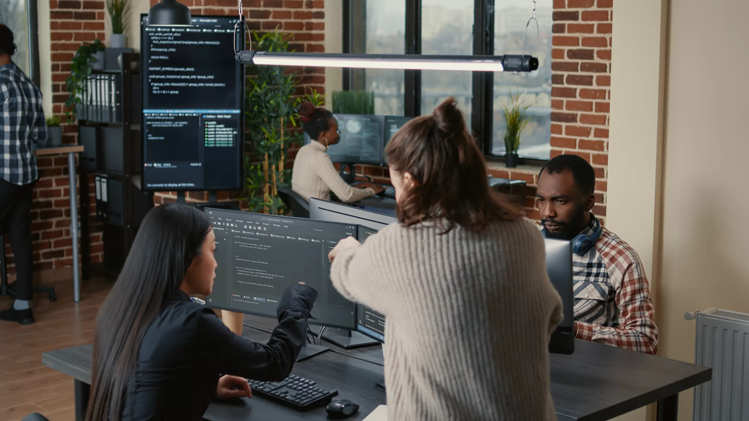 Group of developers gathered around multiple monitors, discussing and reviewing code during a collaborative work session, developing open source code.