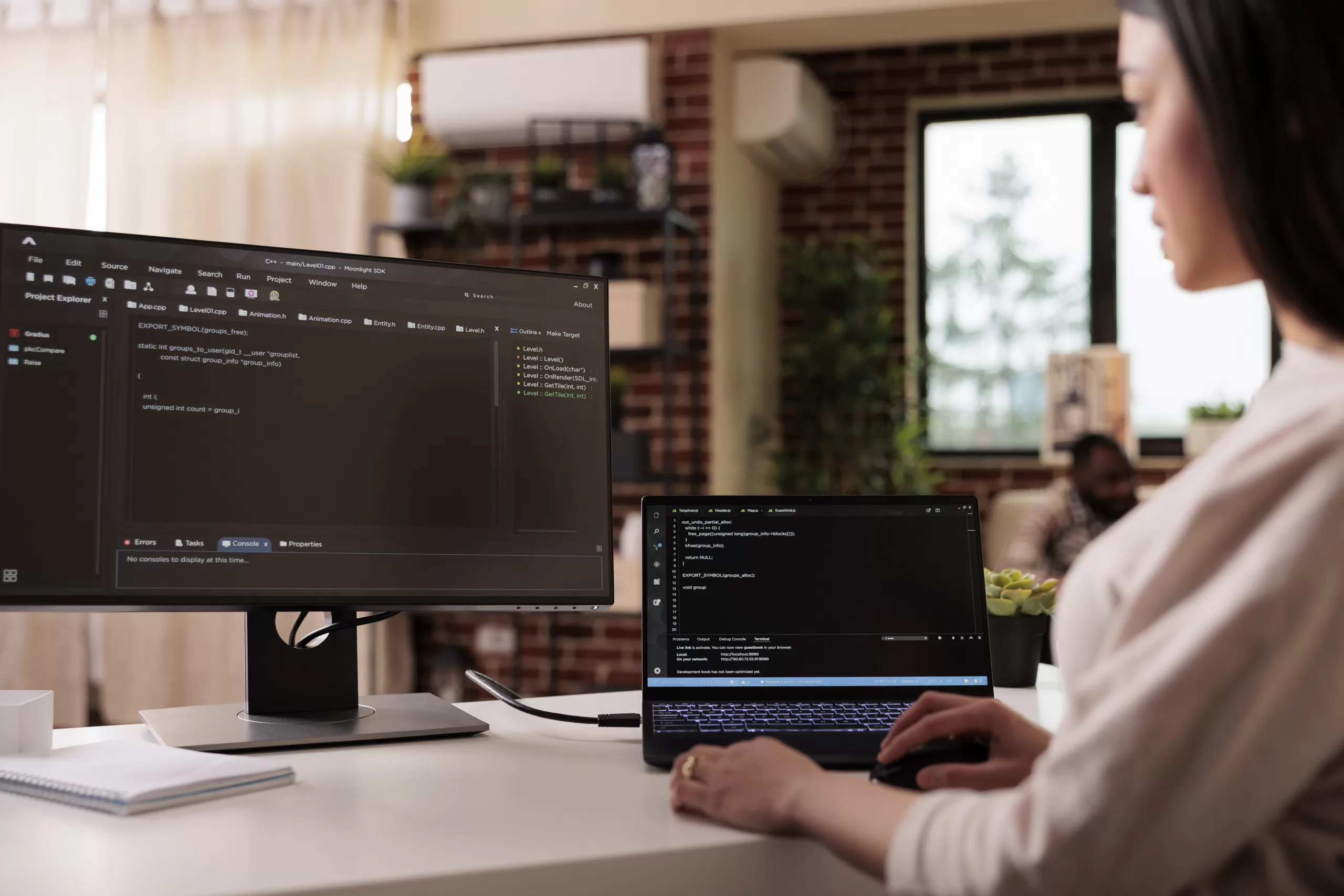 Mulher programando em ambiente de trabalho com dois monitores, escrevendo códigos.