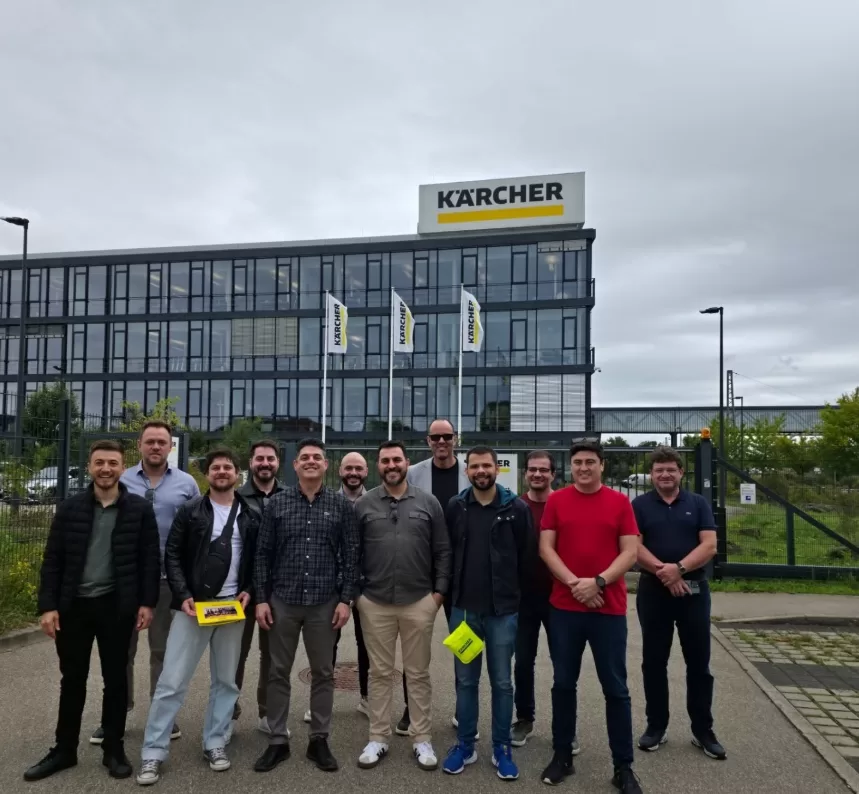 Marcelo Ferri, CEO da NextAge, em frente ao prédio da sede da Kärcher na Alemanha, posando para foto com o logotipo e as bandeiras da empresa ao fundo.