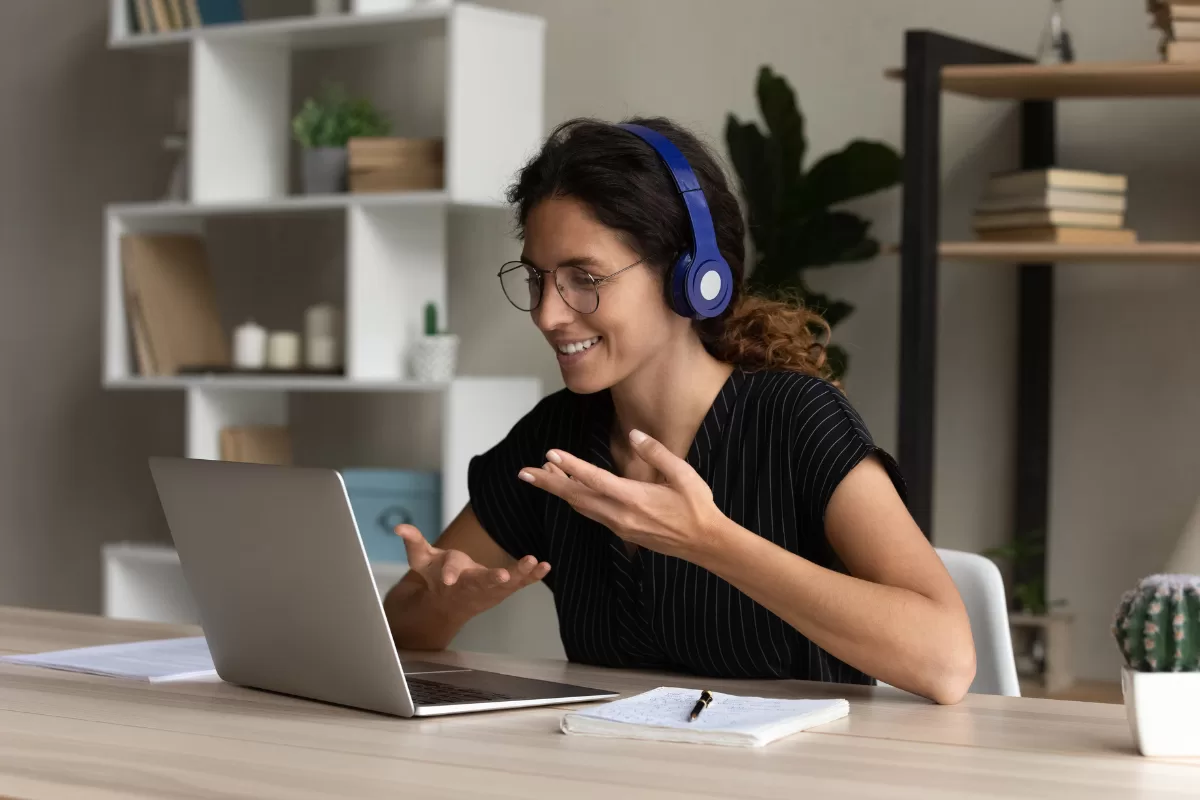 Profissional de TI em reunião remota, usando fones e notebook, gesticulando durante a chamada de vídeo.