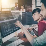 Dois desenvolvedores analisando código em um monitor grande em ambiente de escritório colaborativo, representando empresas para desenvolvimento em Java