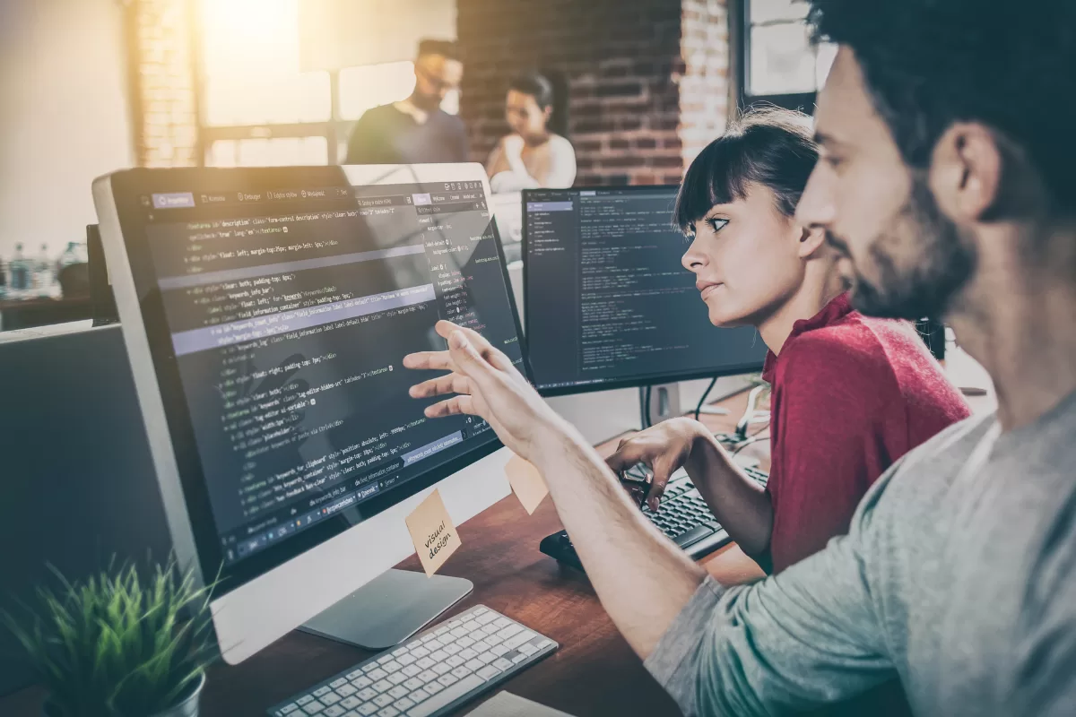 Dois desenvolvedores analisando código em um monitor grande em ambiente de escritório colaborativo, representando empresas para desenvolvimento em Java
