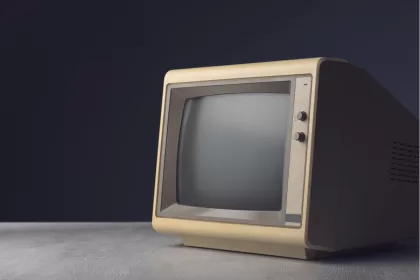 Monitor CRT vintage bege dos anos 80/90 com tela apagada sobre mesa de madeira com fundo escuro, representando tecnologia desatualizada