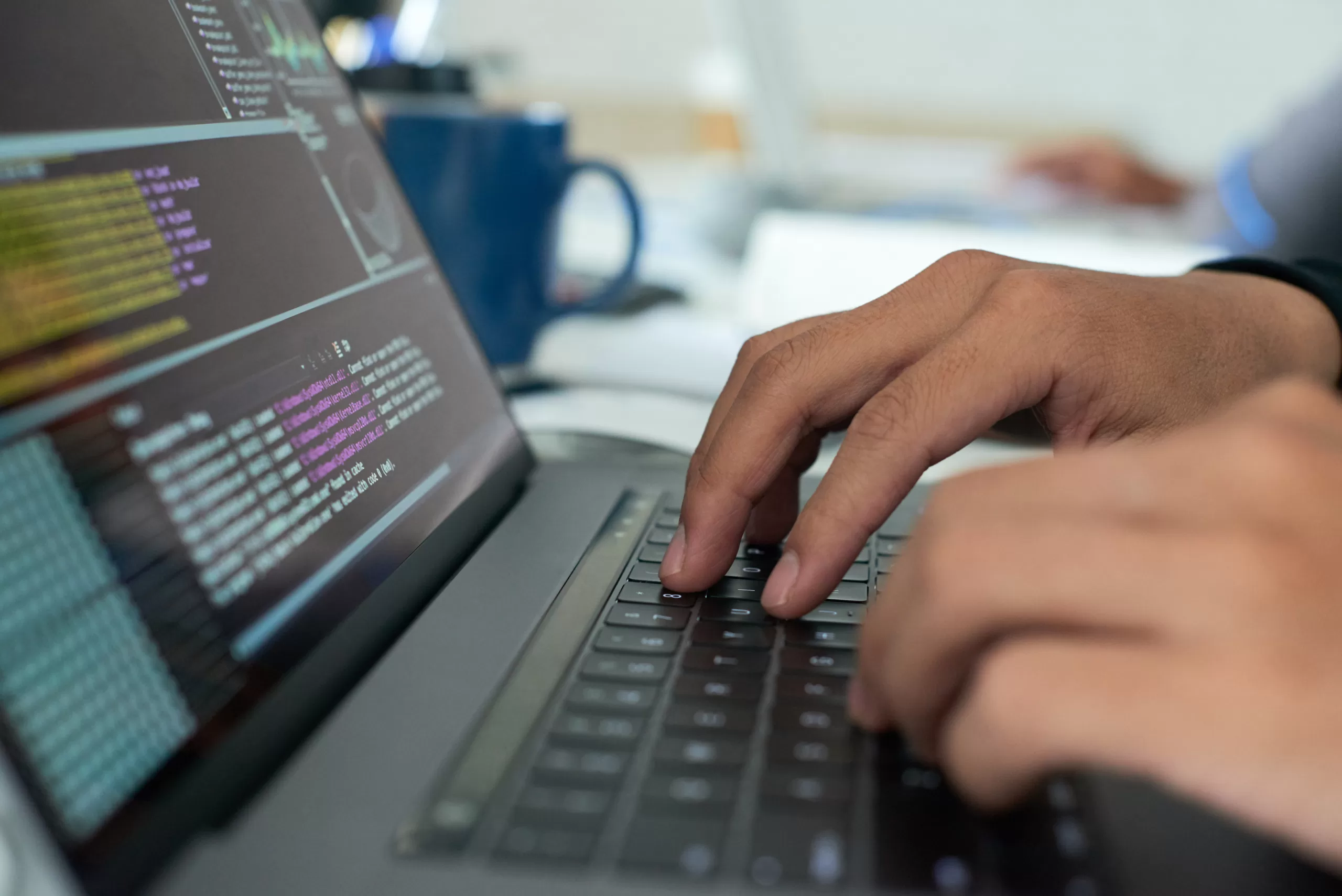 Mãos de um programador digitando código em um laptop durante o desenvolvimento de software.