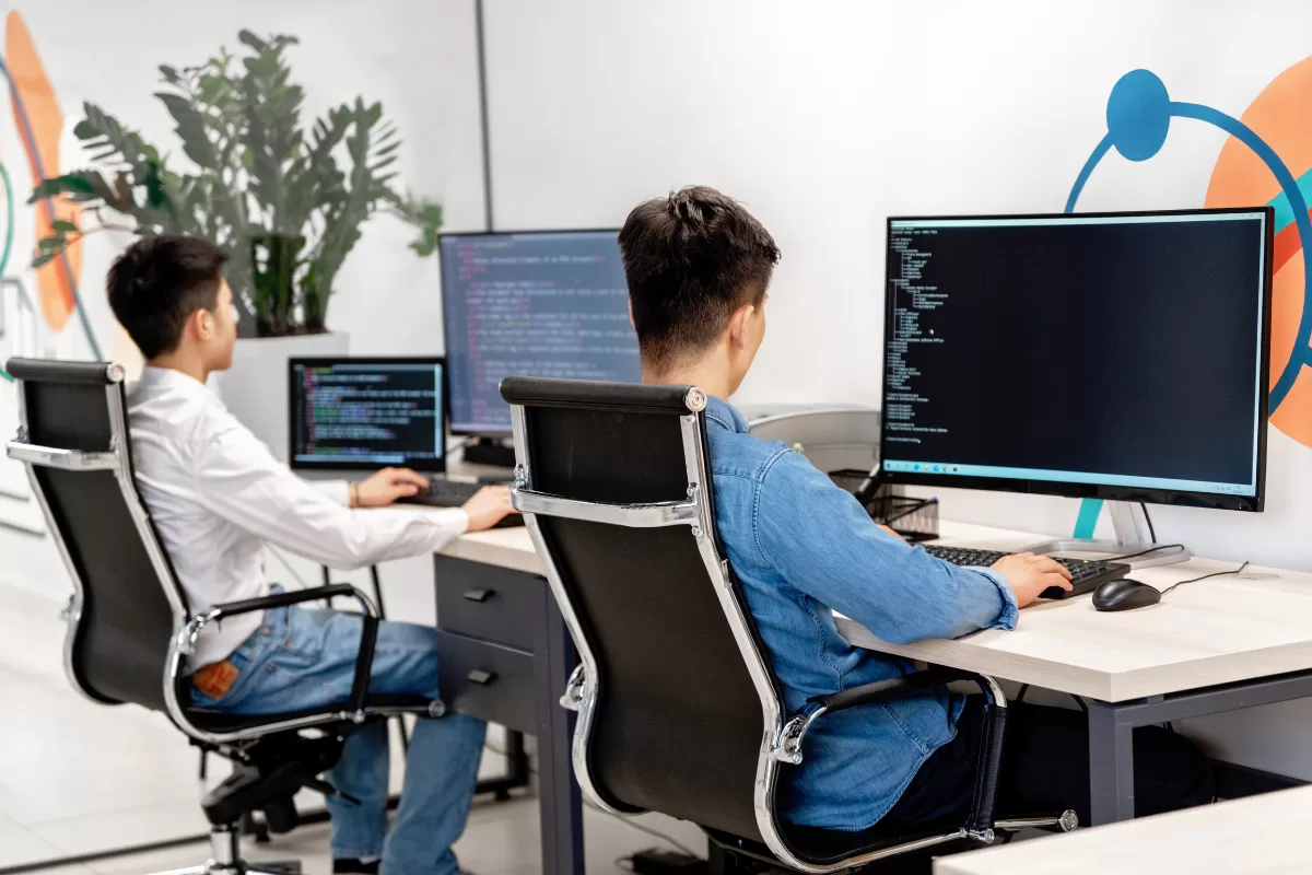 Mão digitando em um notebook com um editor de código aberto sobre uma mesa de madeira.
