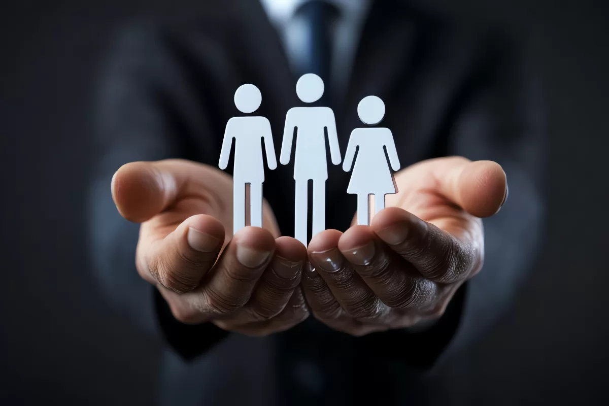 Hands of a person in a suit carefully holding three small, stylized white figures representing people, suggesting onboarding or team care.