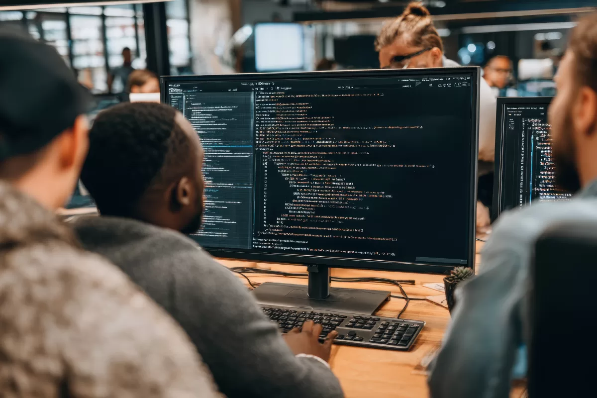 Monitor displaying programming code in foreground with development team working collaboratively in background at office environment