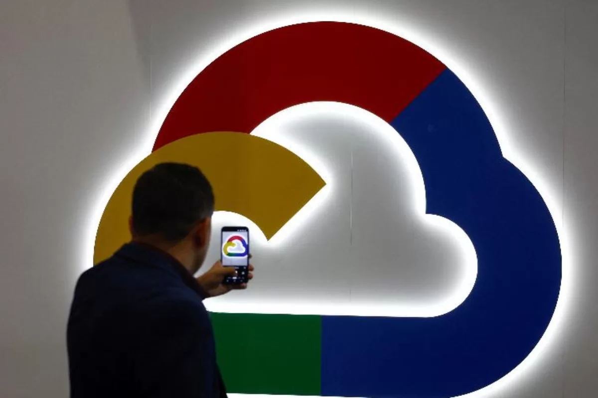 Man taking a photo of the colorful Google Cloud logo illuminated on a tech booth wall.