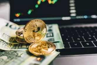 Moedas de bitcoin douradas sobre notas de euro em teclado de laptop com gráficos financeiros desfocados ao fundo na tela