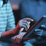 Desenvolvedor trabalhando em laptop com código de programação na tela em ambiente de desenvolvimento integrado (IDE) com iluminação azul ao fundo representando tendências da tecnologia