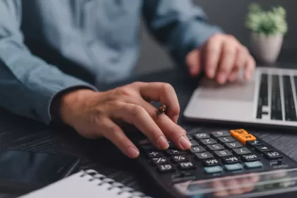 Mãos de profissional usando calculadora enquanto trabalha no laptop, simbolizando cálculo de custos e planejamento financeiro de TI