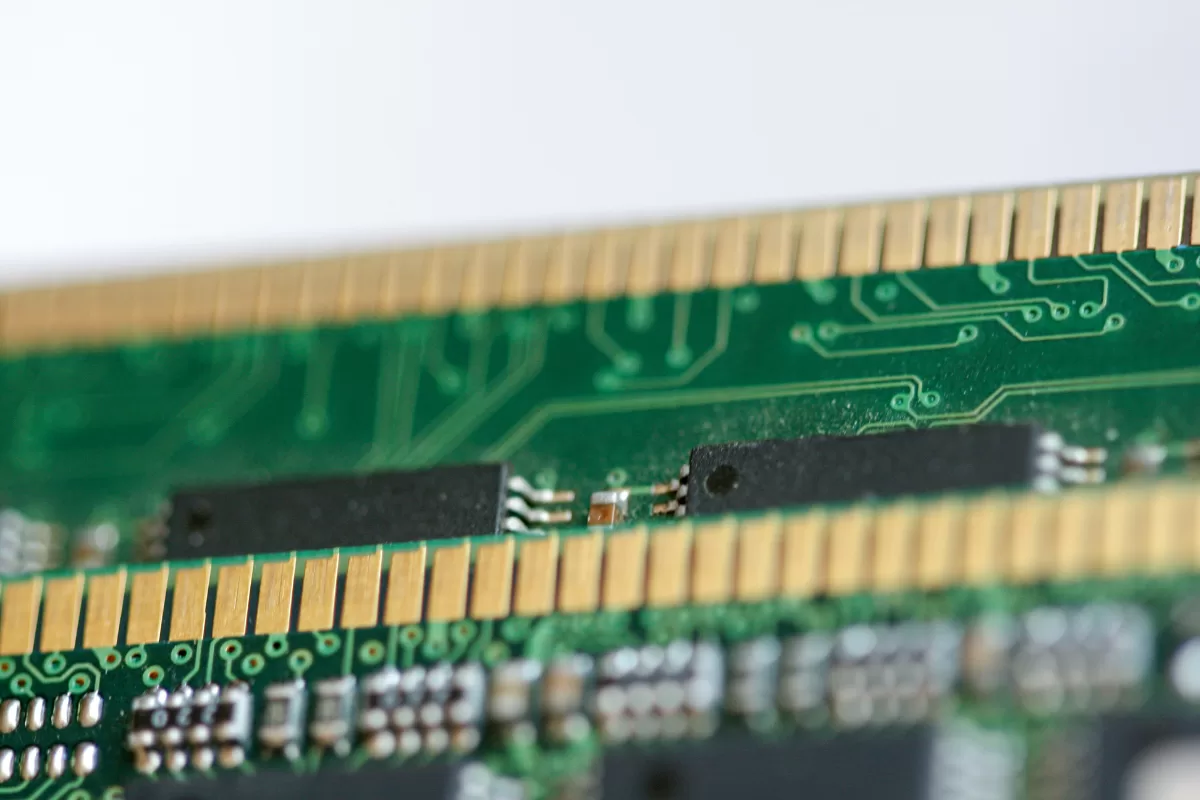 A macro shot focusing on the golden contacts and a portion of a green circuit board from a DRAM (Dynamic Random-Access Memory) module, showing some small components.