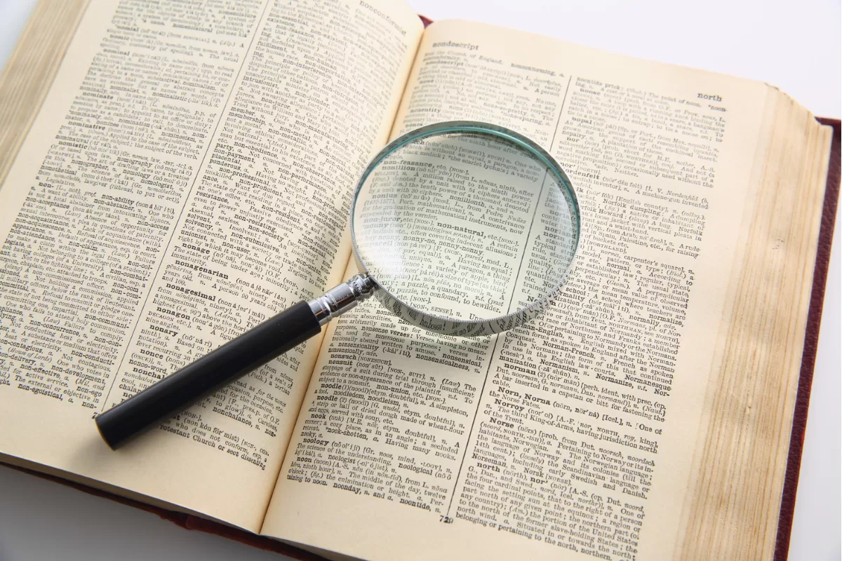 Magnifying glass on an open dictionary, enlarging words on the page.
