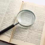 Lupa sobre um dicionário aberto, ampliando palavras na página. Imagem que representa o dicionário de IA.