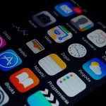 Tela de smartphone exibindo diversos aplicativos organizados, incluindo App Store, Wallet, Mapy e outros ícones de interface móvel sobre fundo escuro