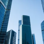 Vista de baixo para cima de edifícios corporativos modernos com fachadas de vidro azul em centro empresarial, representando empresas de desenvolvimento de software