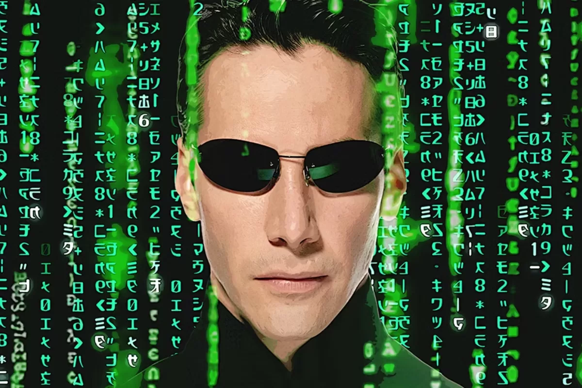 Neo, personagem principal de Matrix, aparece de óculos escuros com códigos verdes caindo ao fundo. Isso representa 5 tecnologias de filmes que existem na vida real