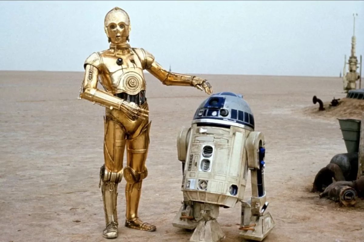 C-3PO e R2-D2, dois robôs icônicos de Star Wars, estão juntos em um deserto.
