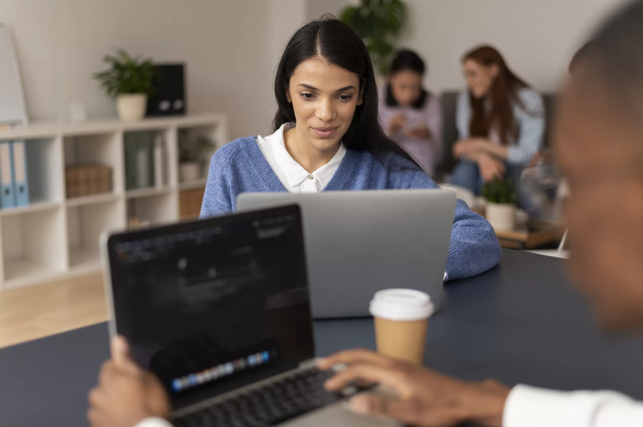 Desenvolvedora trabalhando em laptop em ambiente de escritório colaborativo com equipe ao fundo