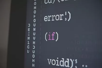 Close-up em uma tela de computador exibindo linhas de código de programação em uma interface de desenvolvimento escura. O texto mostra termos como "error", "if" e "void" com destaque em cores diferentes.