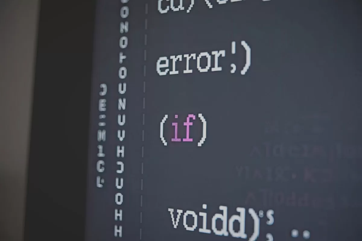 Close-up em uma tela de computador exibindo linhas de código de programação em uma interface de desenvolvimento escura. O texto mostra termos como "error", "if" e "void" com destaque em cores diferentes.