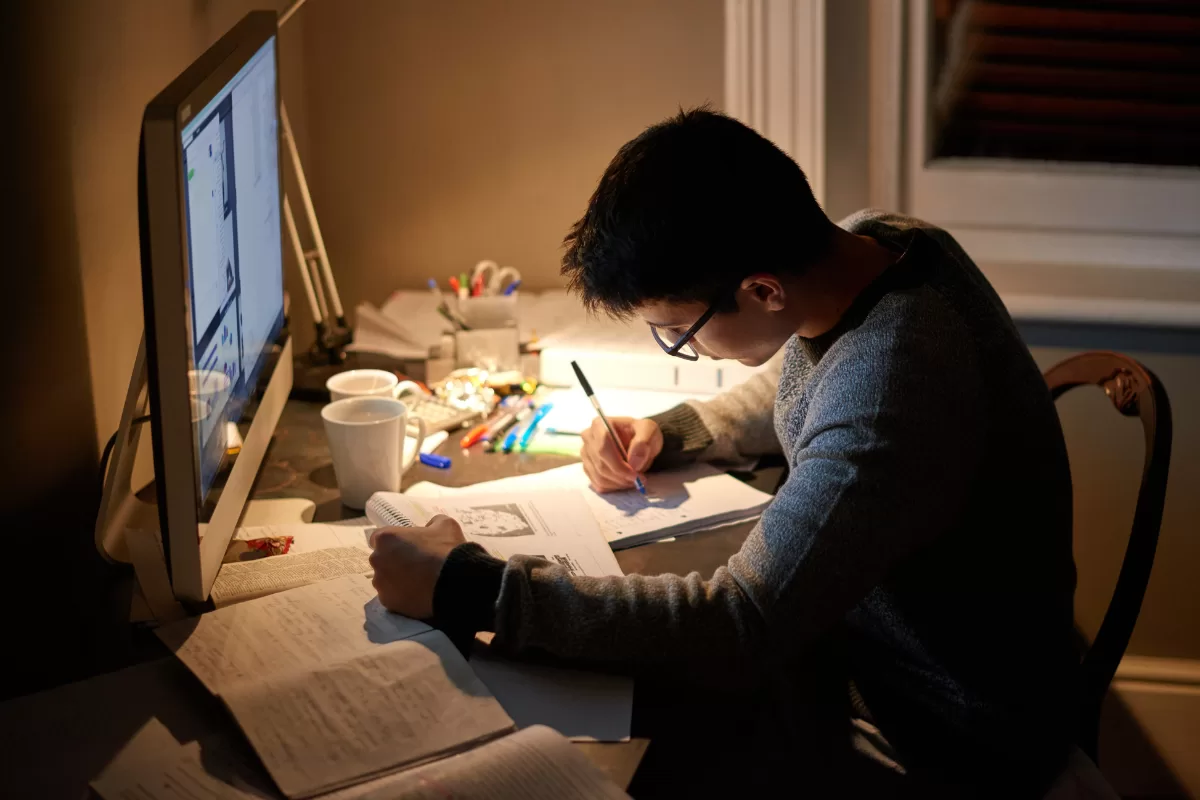 IT professional studying and taking notes in front of computer at night, representing the dedication needed to become a software engineer