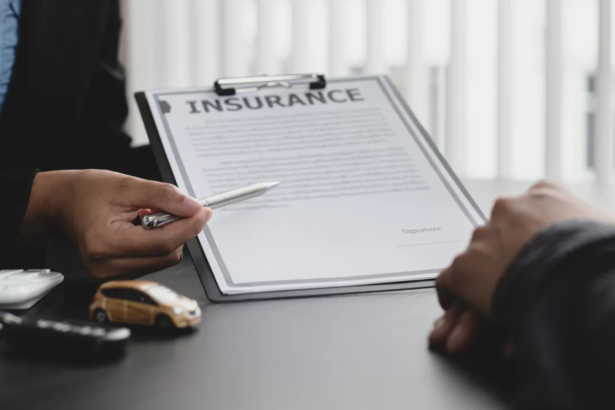 Insurance professional presenting policy contract on clipboard for client to sign, with miniature car beside symbolizing auto insurance