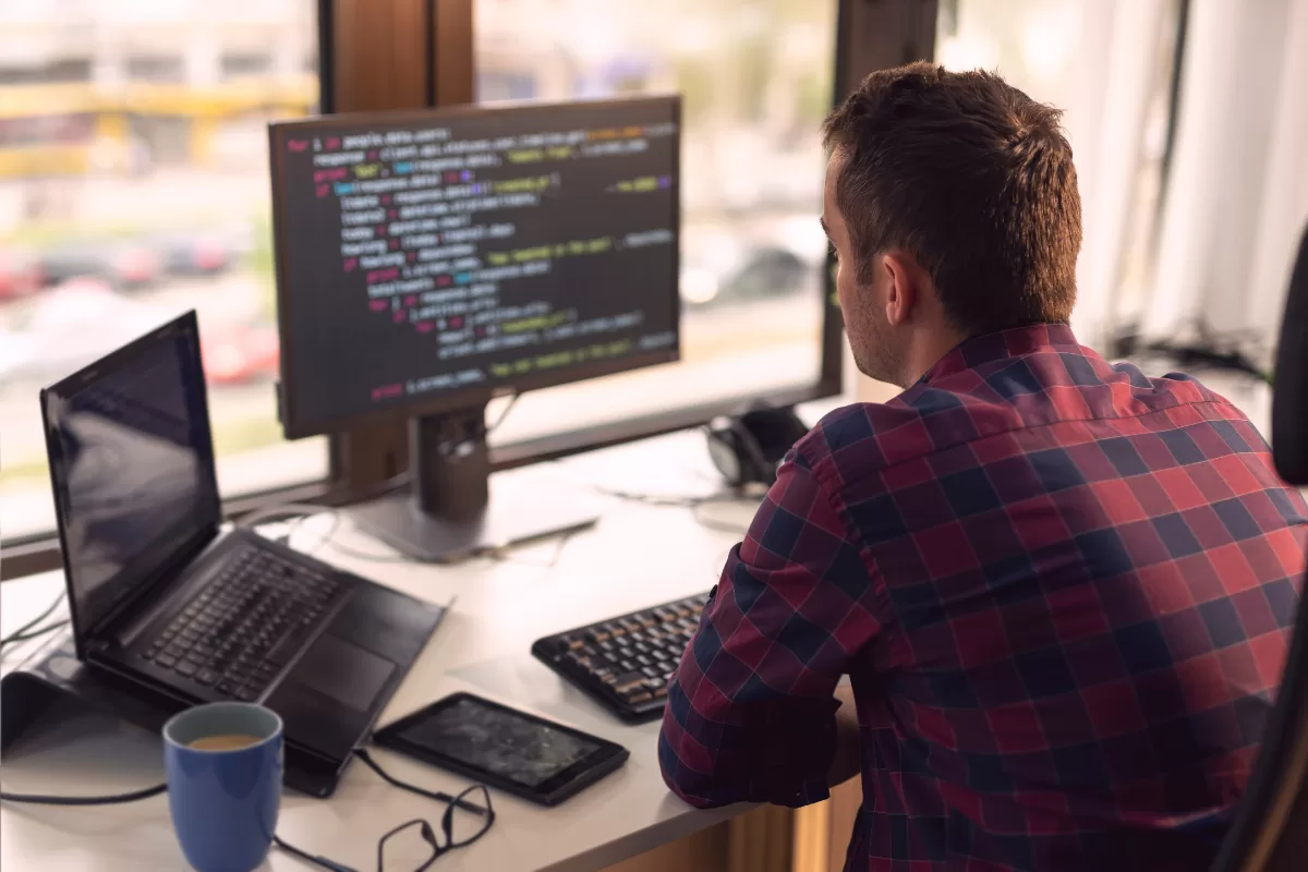 Full stack developer working on code on monitor while using laptop, representing the daily routine of a technology professional