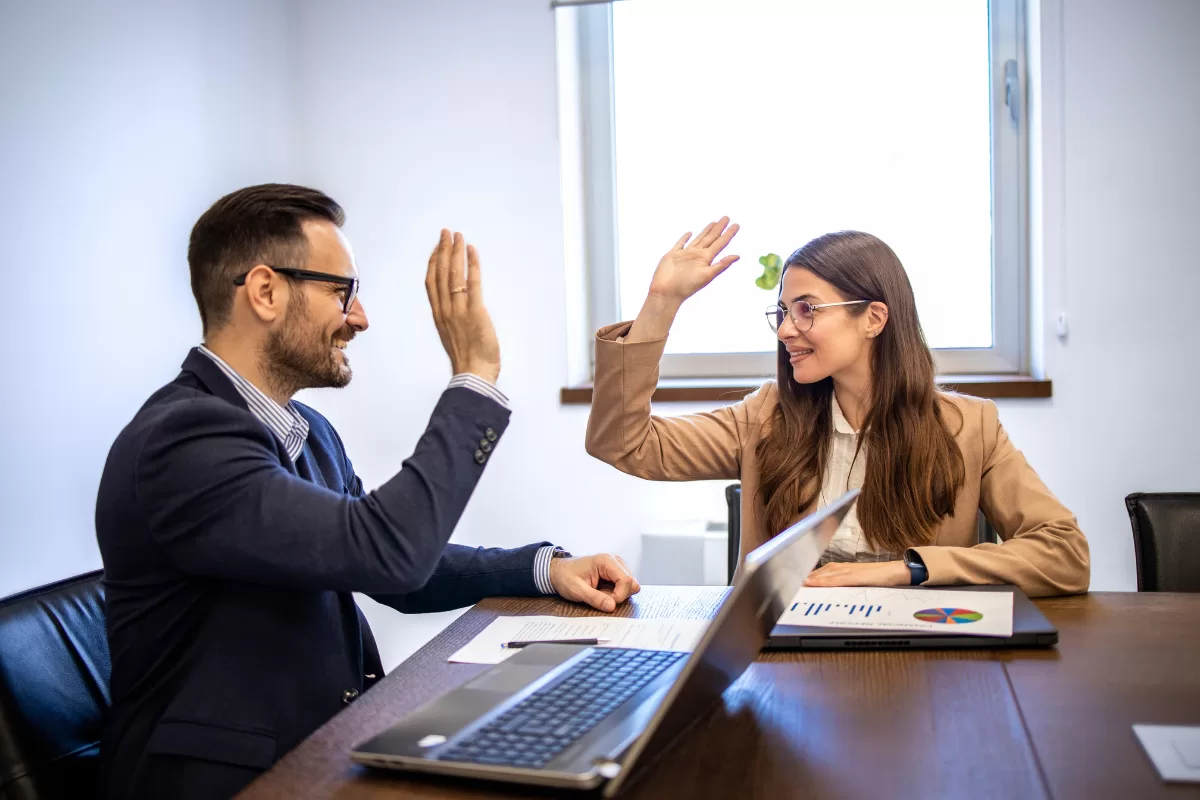 Two business professionals celebrating agreement with high-five in corporate environment during technology project meeting