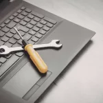 Chave de fenda e chave inglesa sobre teclado de laptop, simbolizando ferramentas de manutenção e suporte técnico para sustentação de sistemas de TI.
