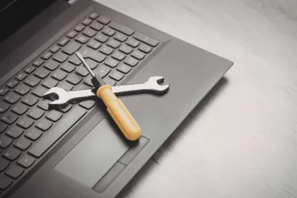 Chave de fenda e chave inglesa sobre teclado de laptop, simbolizando ferramentas de manutenção e suporte técnico para sustentação de sistemas de TI.