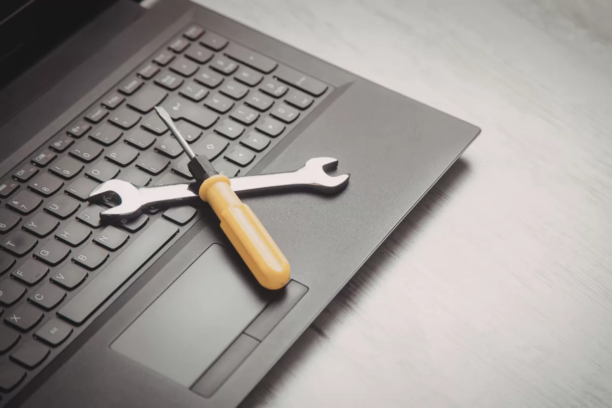 Chave de fenda e chave inglesa sobre teclado de laptop, simbolizando ferramentas de manutenção e suporte técnico para sustentação de sistemas de TI.