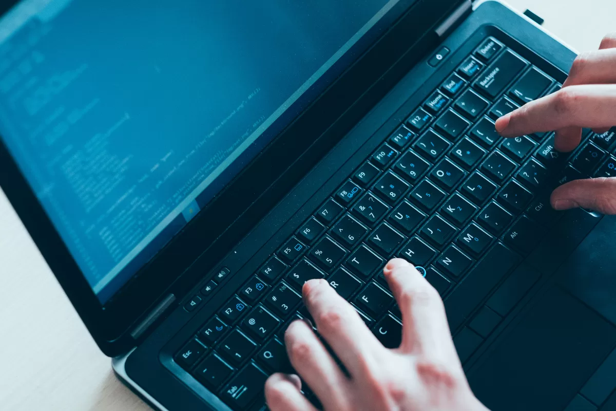 Hands typing on a laptop with a screen displaying lines of code in a terminal environment.