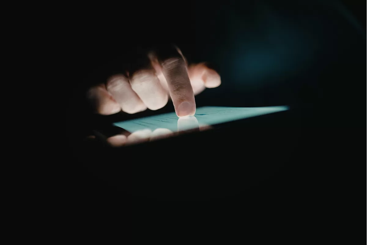 Hand touching the glowing screen of a tablet in a dark environment, representing mobile app usage