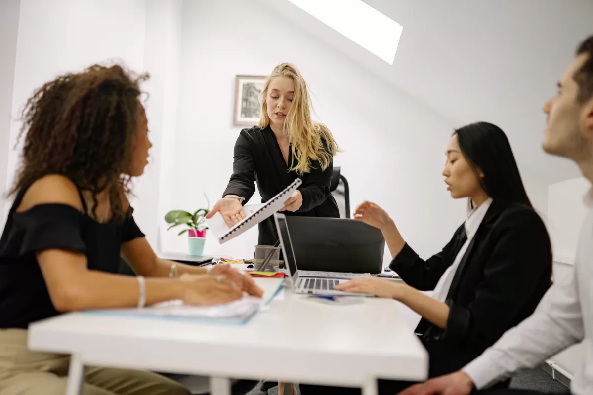 A tech lead presents content on a laptop to three colleagues during a team meeting in an office room.