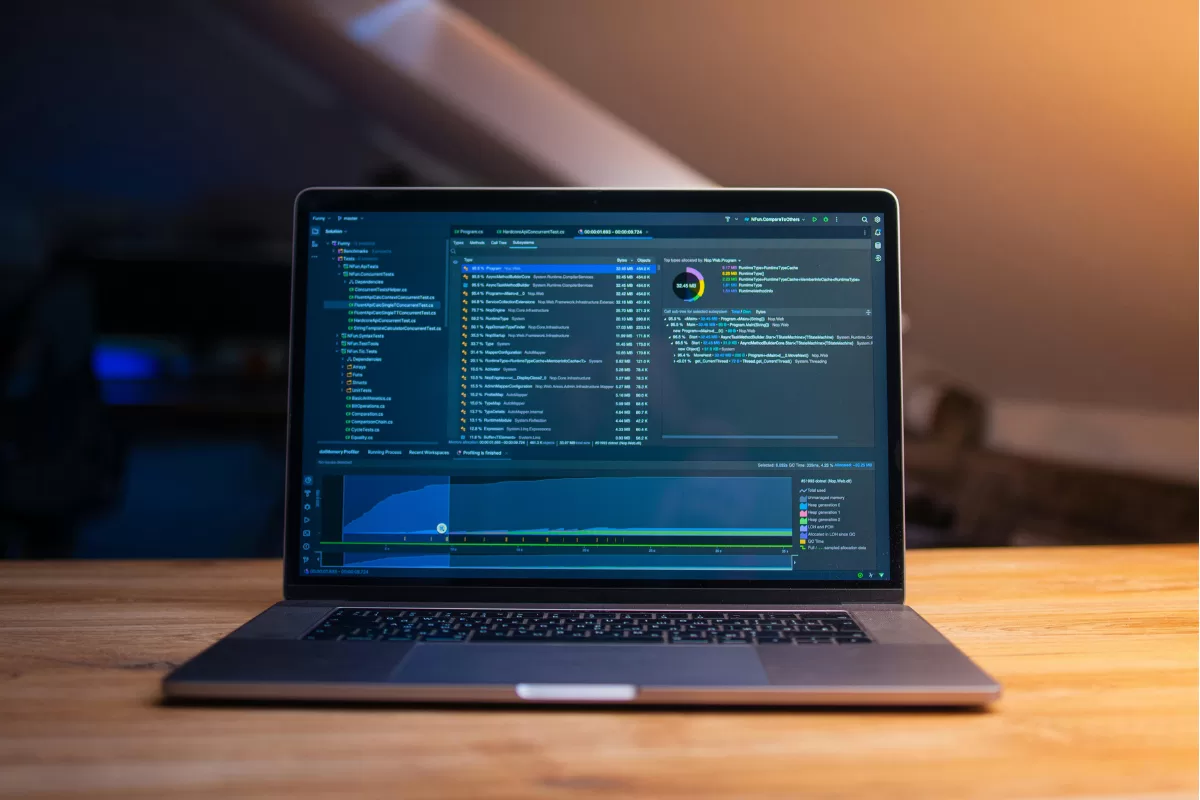Notebook sobre mesa de madeira com IDE aberta exibindo código e ferramenta de profiling de memória em execução, representando desenvolvimento de software em andamento.