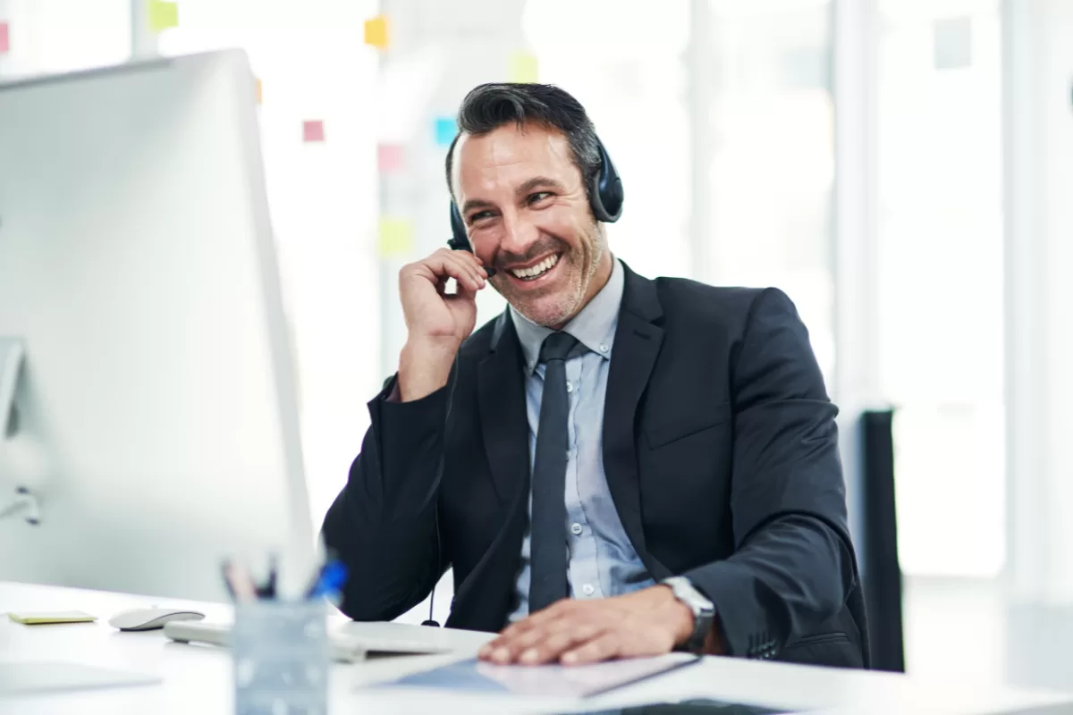 Smiling sales professional talking on a headset in front of a computer in a modern office